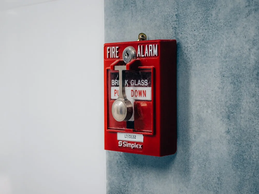 Estación manual de alarma con tapa de vidrio instalada en muro de pasillo
